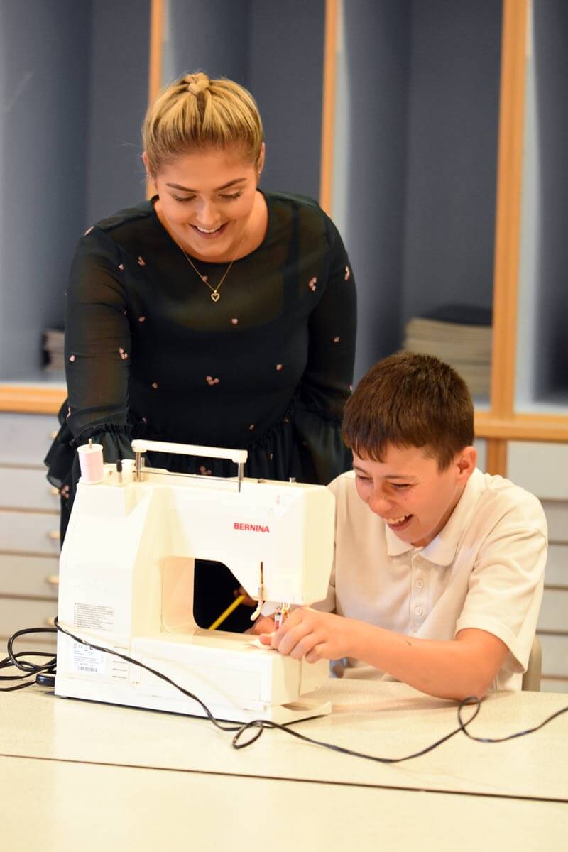 A pupil at a sewing machine with a teacher in the background